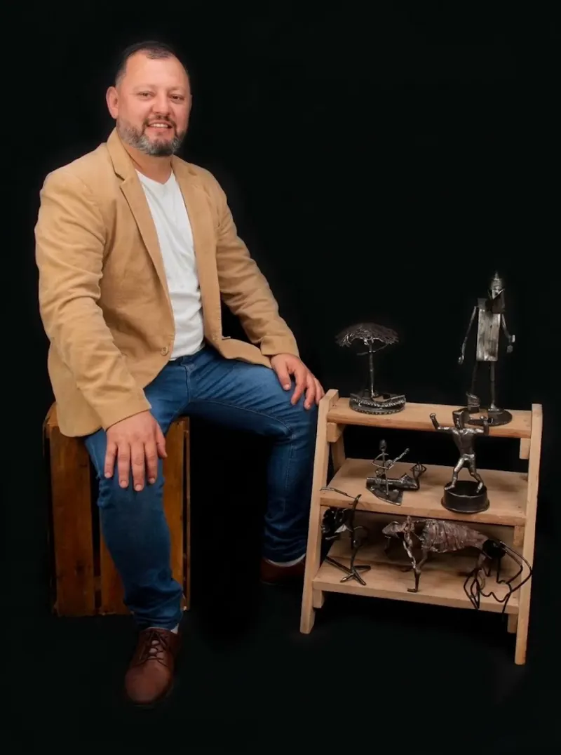 Jaison Bittencourt sentado ao lado de suas esculturas em metal